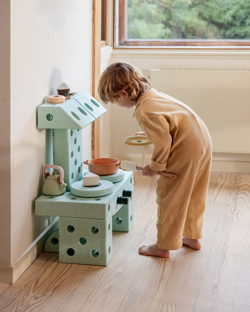 Toddler playing in the living room with MODU play kitchen, built from Dreamer Set in Ocean Mint Forest Green.