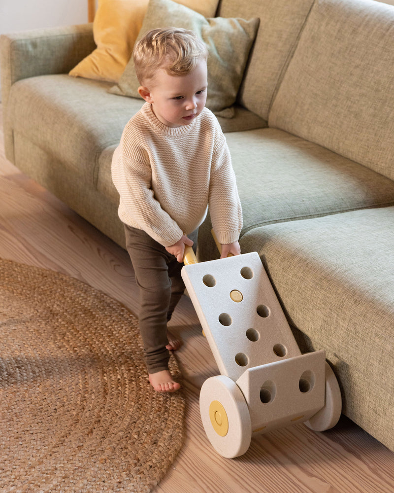Child pushing MODU wheelbarrow, built from Dreamer Set in Sand Grey Honey Yellow. Encourages creative play.