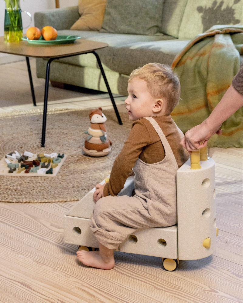Young toddler riding a MODU backrest ride, a ride on toy, built from an Explorer Set in the colour Sand Grey Honey Yellow.