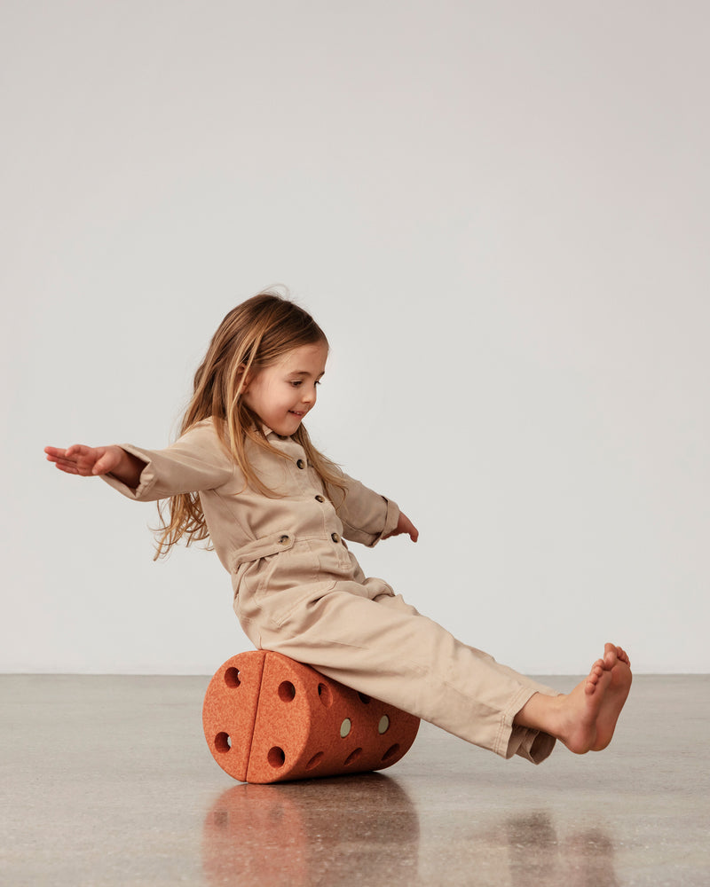 Toddler sitting on MODU Roller in Burnt Orange Dusty Green, practicing balance.