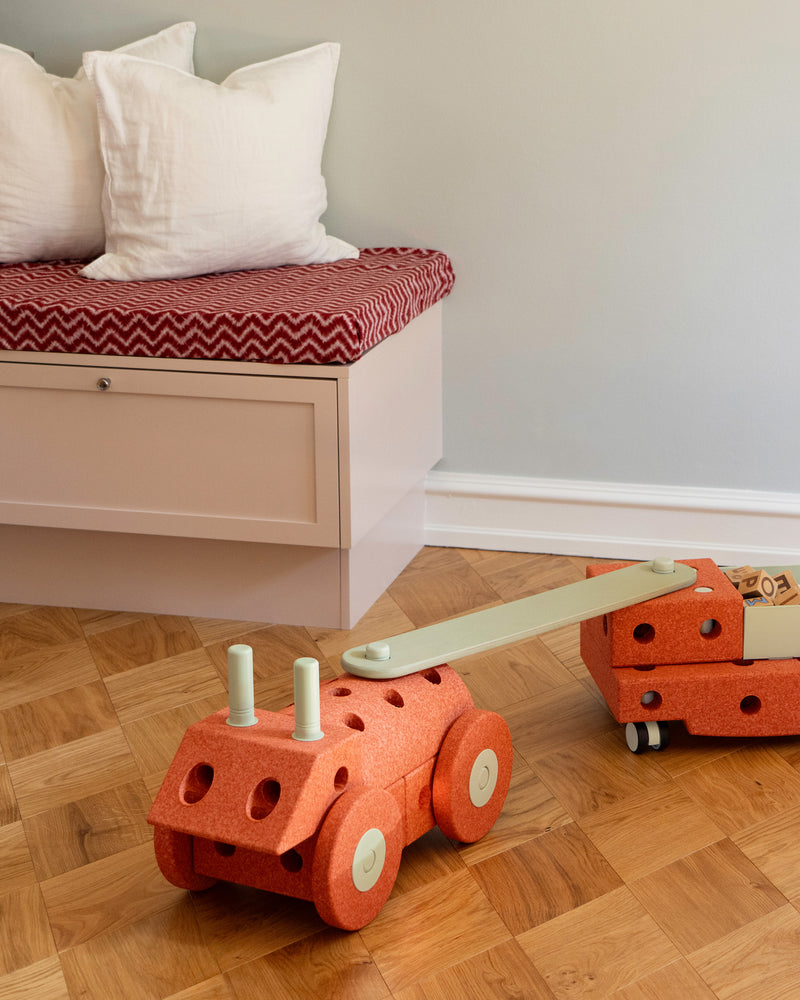 A ride-on with a trailer built from orange MODU foam blocks, connected by a dusty green MODU Balance Beam.