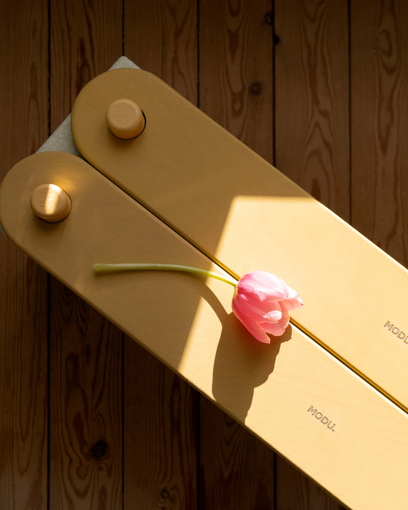 A single pink tulip rests on two honey yellow MODU Balance Beams.