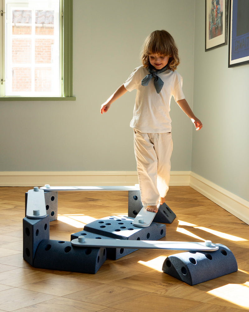 A child walks along an indoor balance track constructed with sky blue MODU Balance Beams in living room.