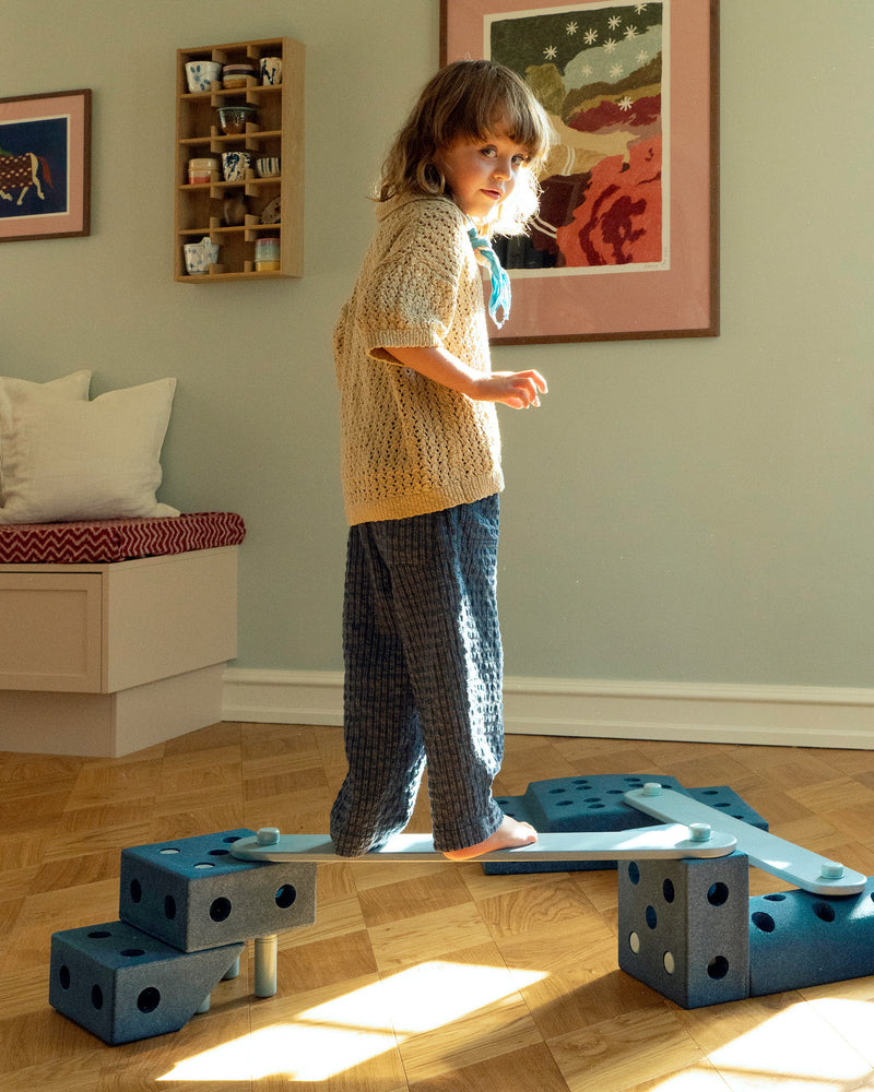 A child balances carefully on a indoor balance track built with sky blue MODU Balance Beams and deep blue MODU building blocks.