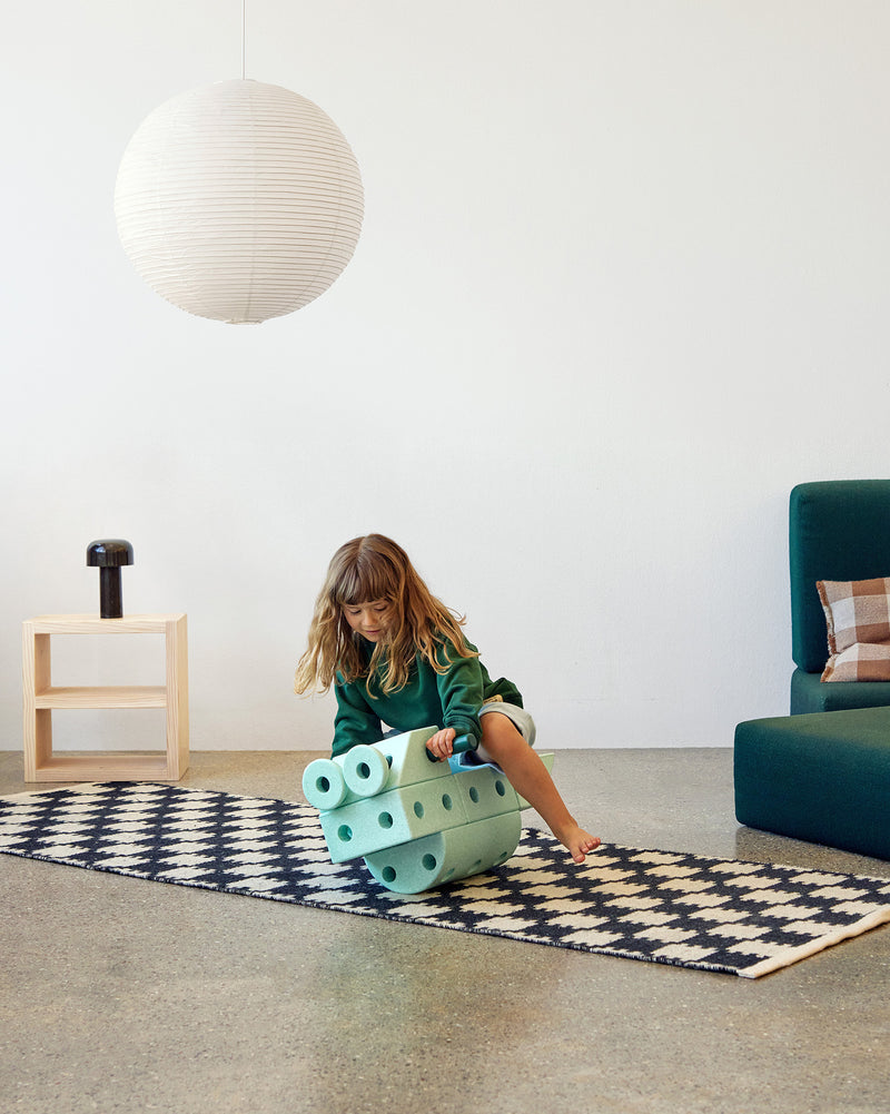 A toddler balancing on a rocking toy build from MODU foam blocks with MODU Foam Balls attached as eyes during active play.