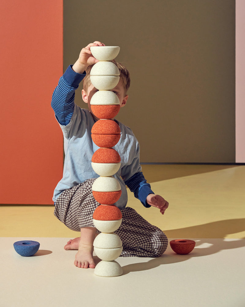 A child builds a tall tower using sand grey and burnt orange MODU Foam Balls, enjoying an engaging building toy activity.