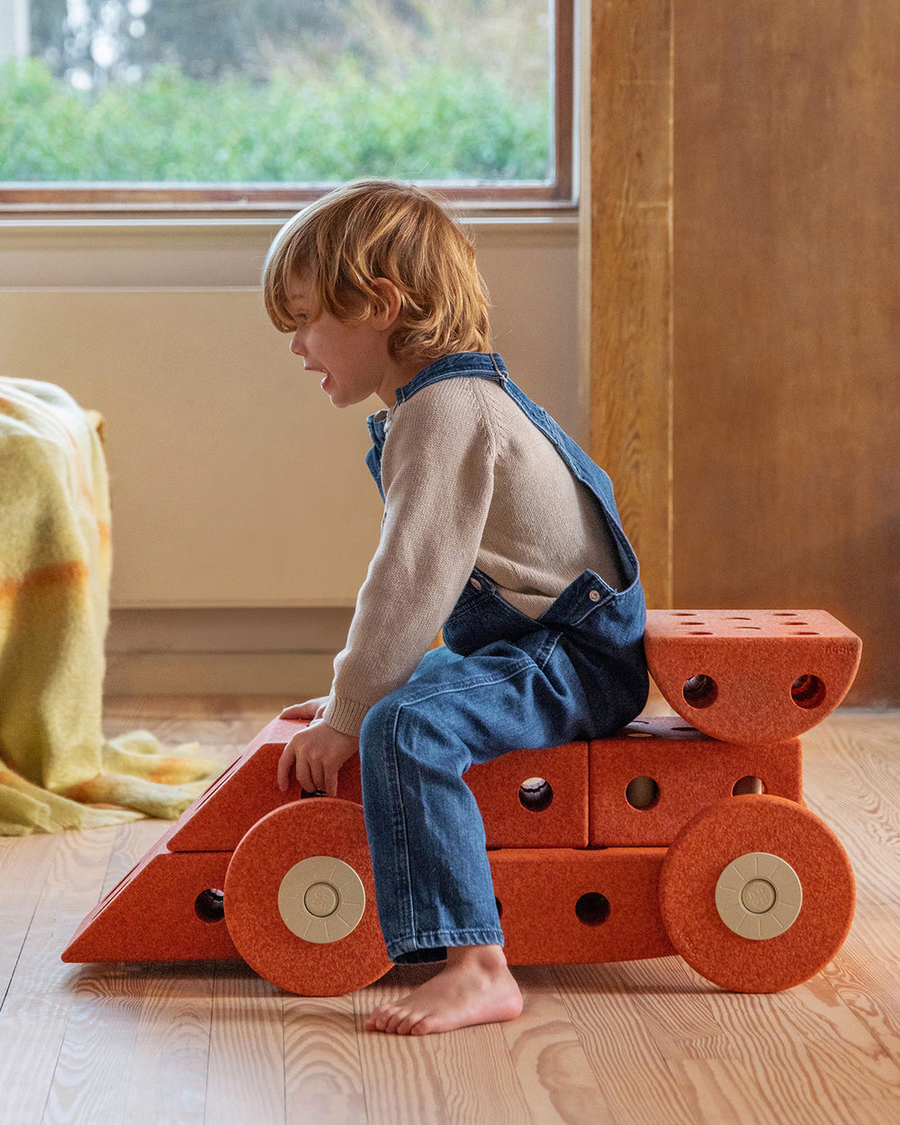 Toddler riding MODU racecar in the kids room. Built from Dreamer Set in the colour Burnt Orange Dusty Green.