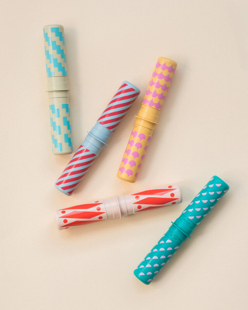 Five colorful rattle pegs with patterned designs on a beige background