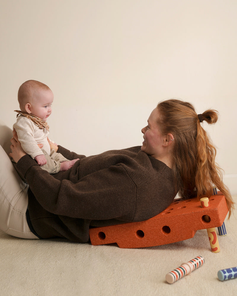 An adult rests back on incline built from the MODU Baby Activity Set while holding a baby in their lap.