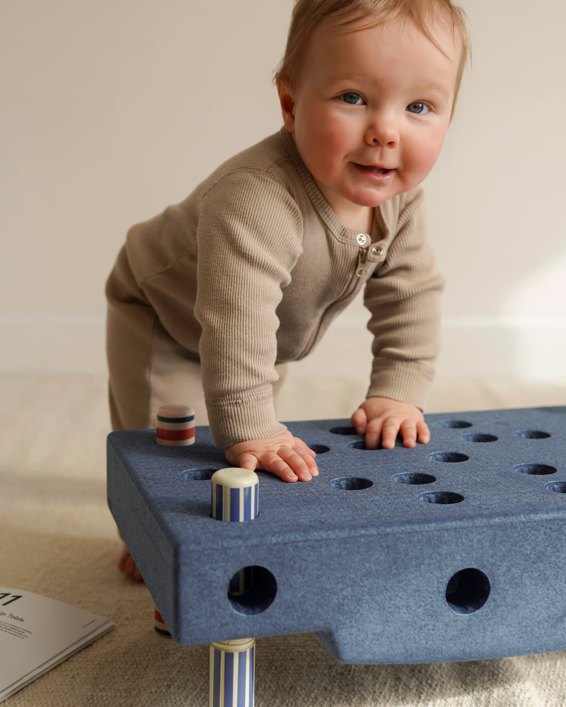 A baby practises standing while leaning on an foam block platform built from the MODU Baby Activity Set.