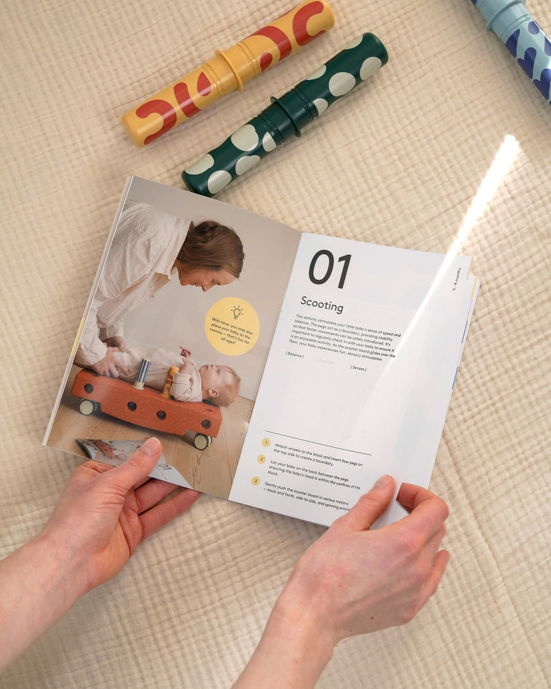 An adult holds open a MODU Activity Guide showing early development play ideas.