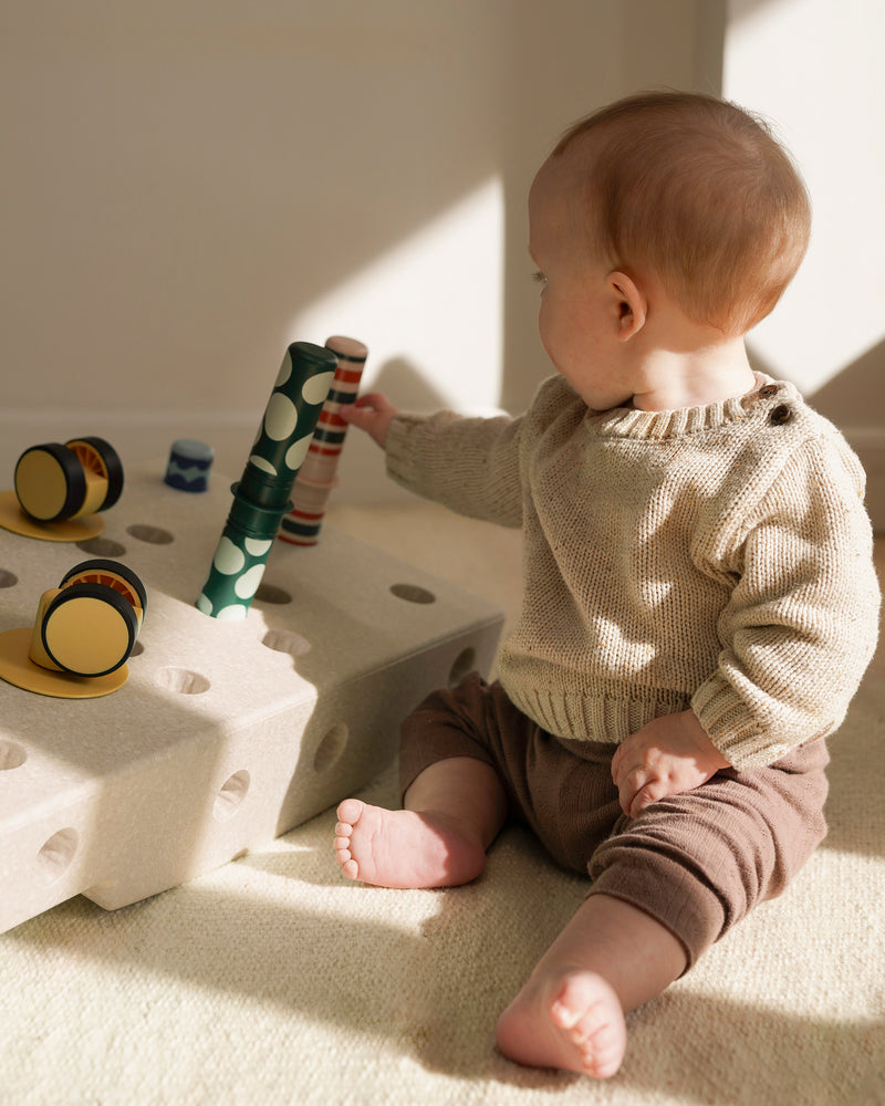 A baby sits on the floor playing with Rattle Pegs placed in MODU base block.