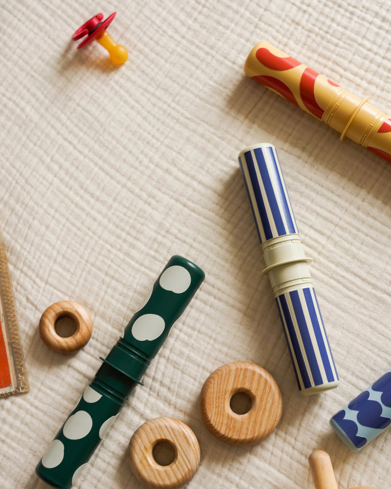 A flat lay view of colorful patterned Rattle Pegs from the MODU Baby Activity Set on a soft muslin blanket.