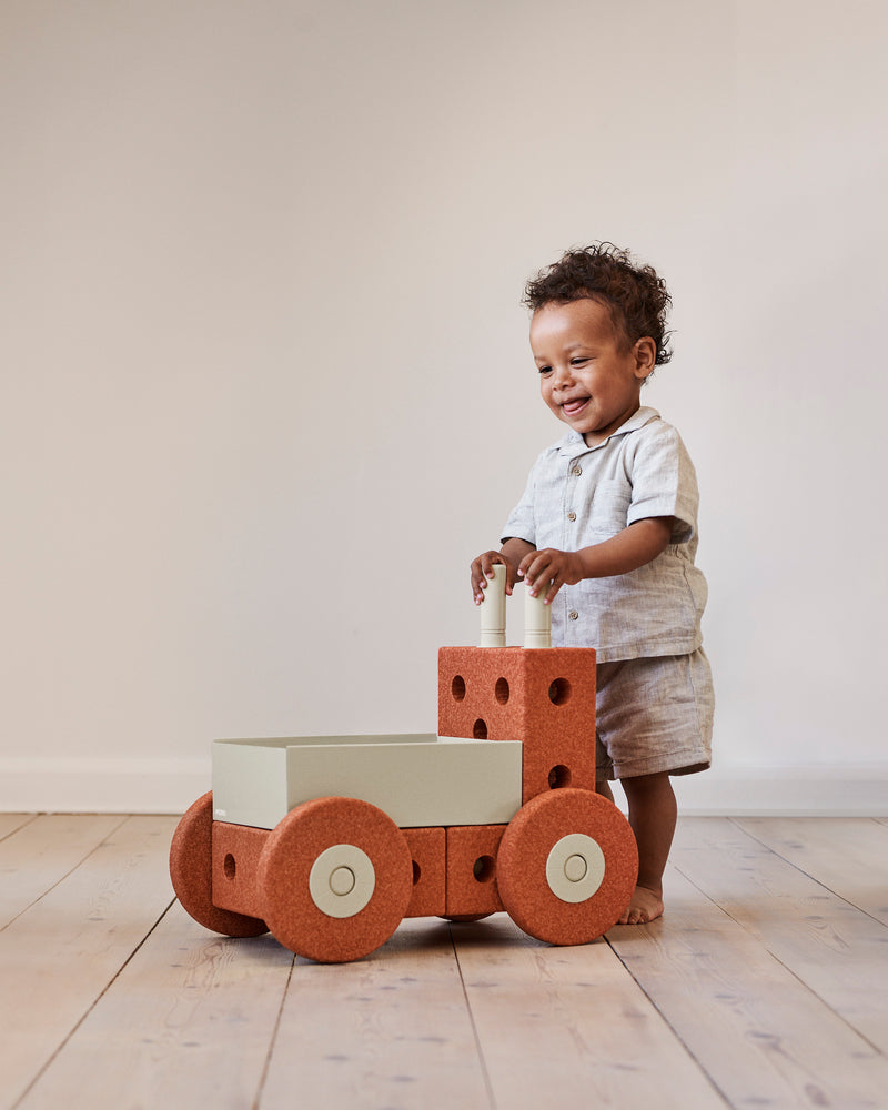 A toddler stands up and holds the handles of a MODU Baby Walker.