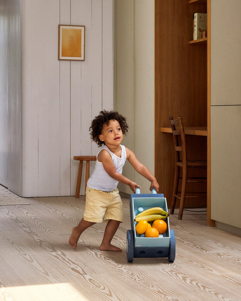 A child pushes a toy wheelbarrow built from the MODU 3-in-1 Baby Walker through a bright living space.