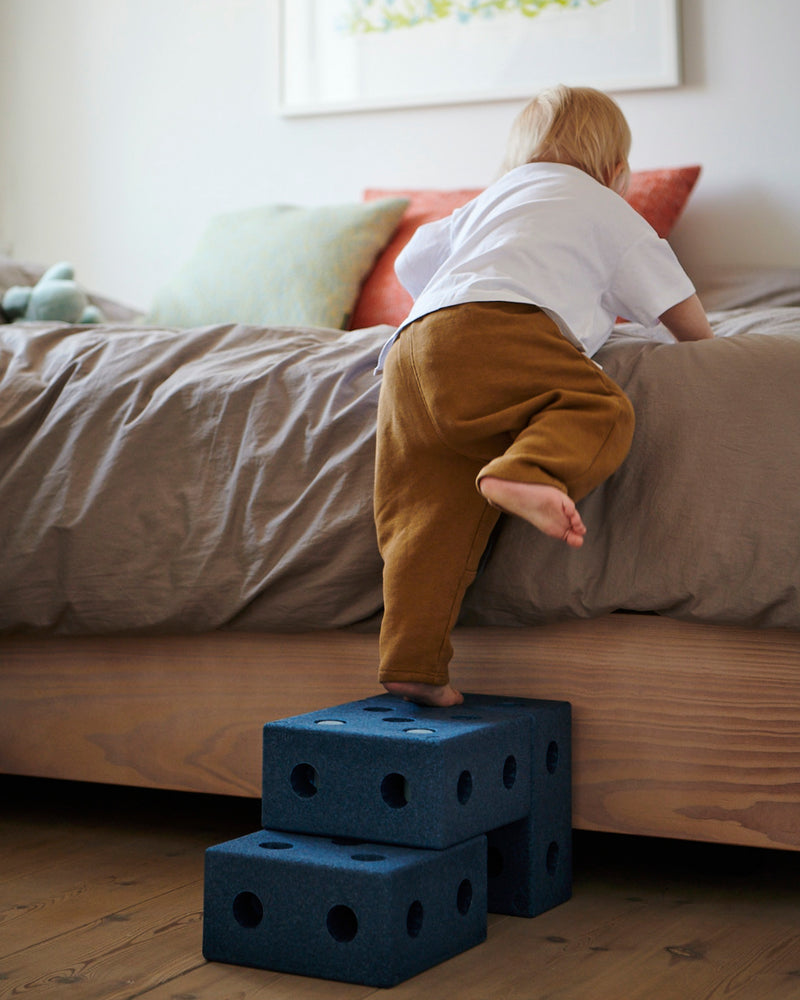 A child climbs onto a bed using a small step stool built from the MODU 3-in-1 Baby Walker in deep blue.