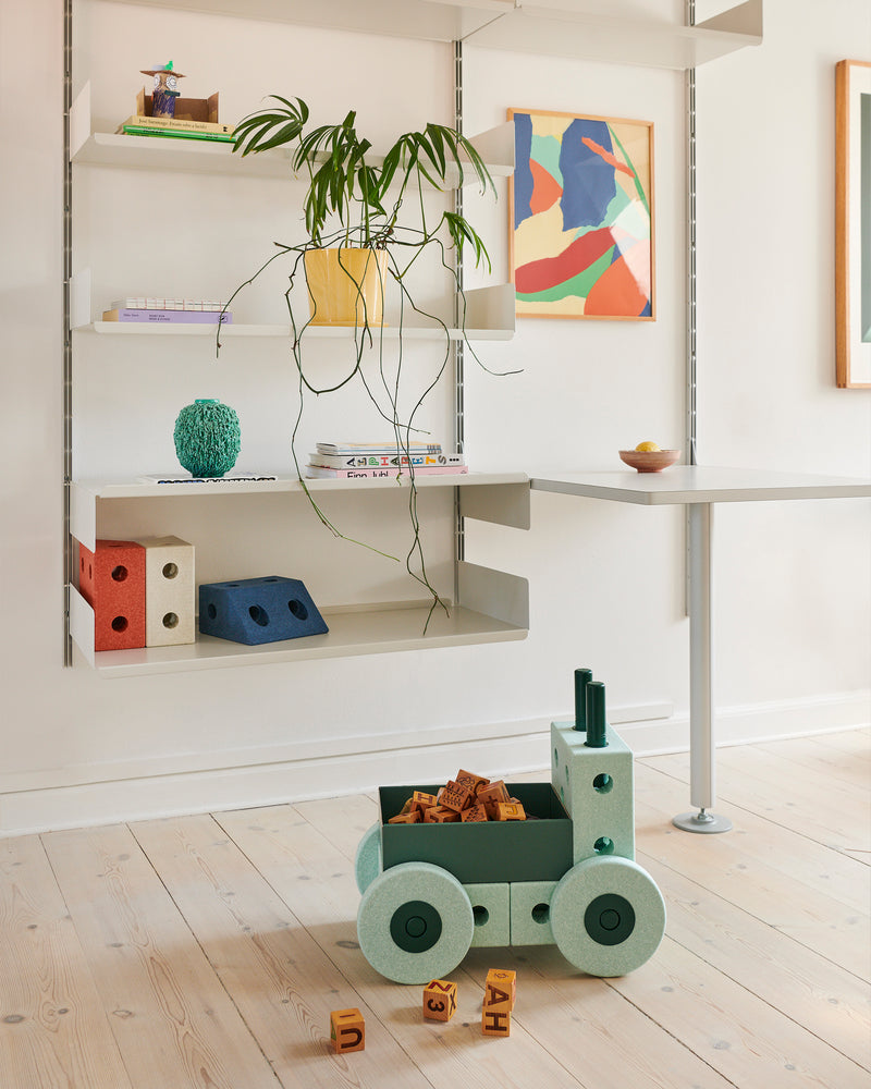 An ocean mint and forest green MODU 3-in-1 Baby Walker with wooden blocks sits on a wooden floor in a bright, Scandinavian-style living room.