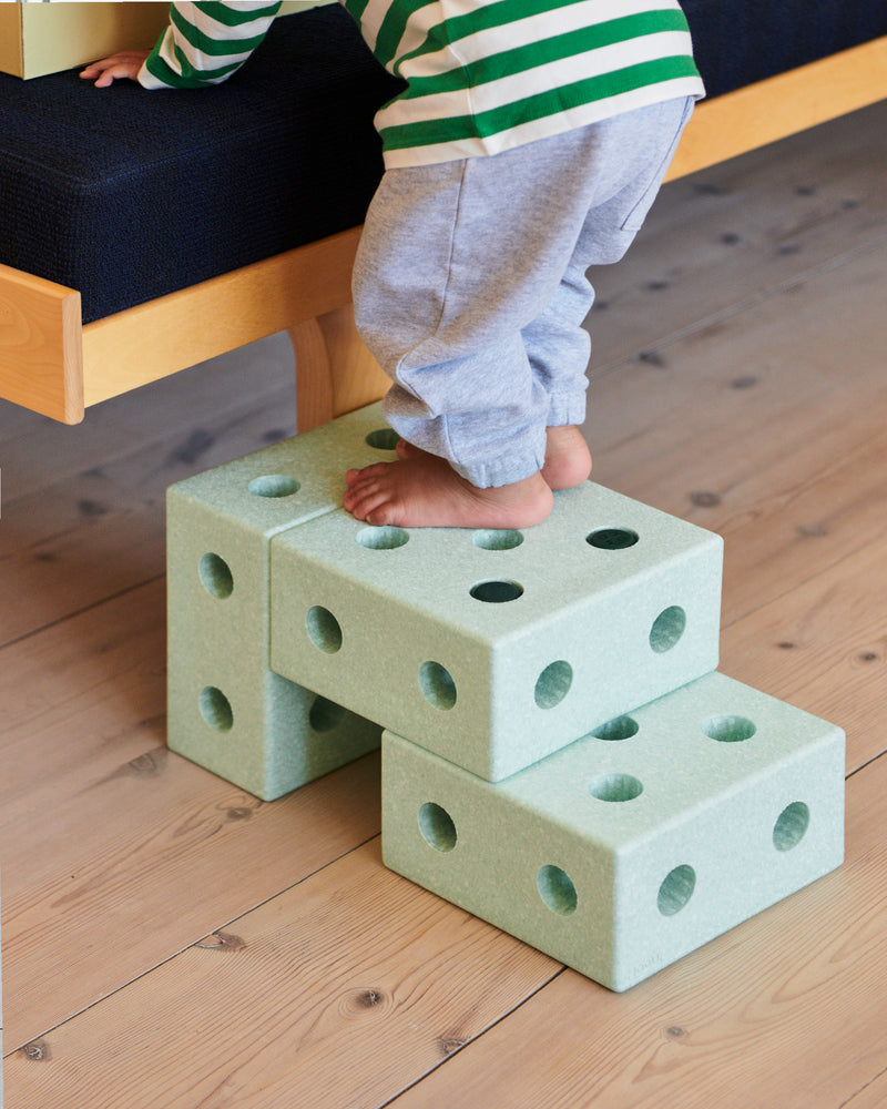 A child climbs onto a small step stool built from the MODU 3-in-1 Baby Walker to get onto a sofa.