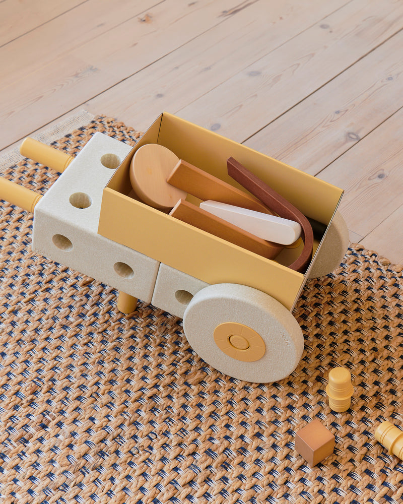 A top-down view of a toy wheelbarrow made from the sand grey and honey yellow MODU Baby Walker, carrying wooden toy blocks.