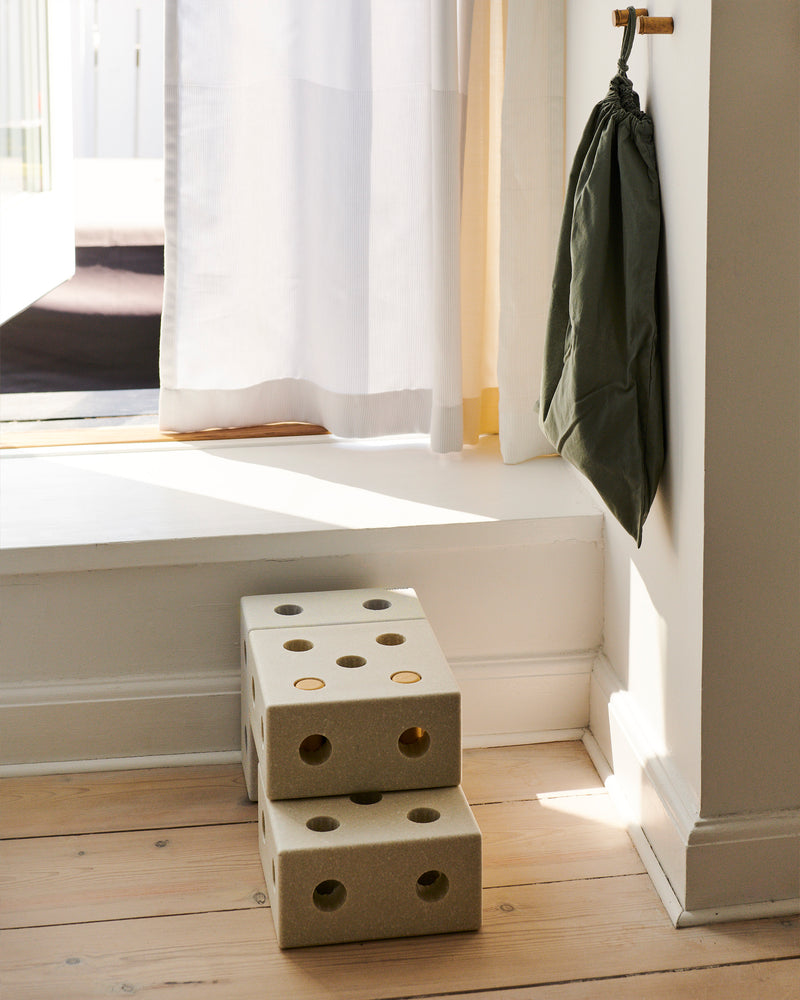 A small step stool build from sand grey MODU foam blocks sits on a wooden floor near a window.