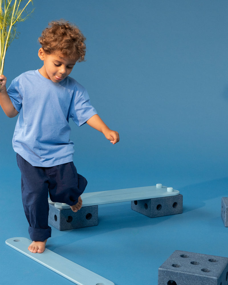 A child balances barefoot while moving along a balance path built with the MODU Balance Track.
