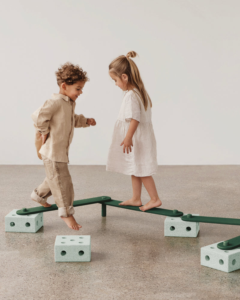 Two children play together, walking and balancing along a MODU Balance Track in ocean mint forrest green.