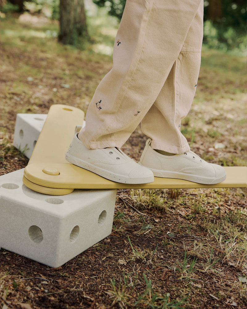 A close-up view of a child's feet in white canvas shoes balancing on a sand grey honey yellow MODU balance track outdoors.