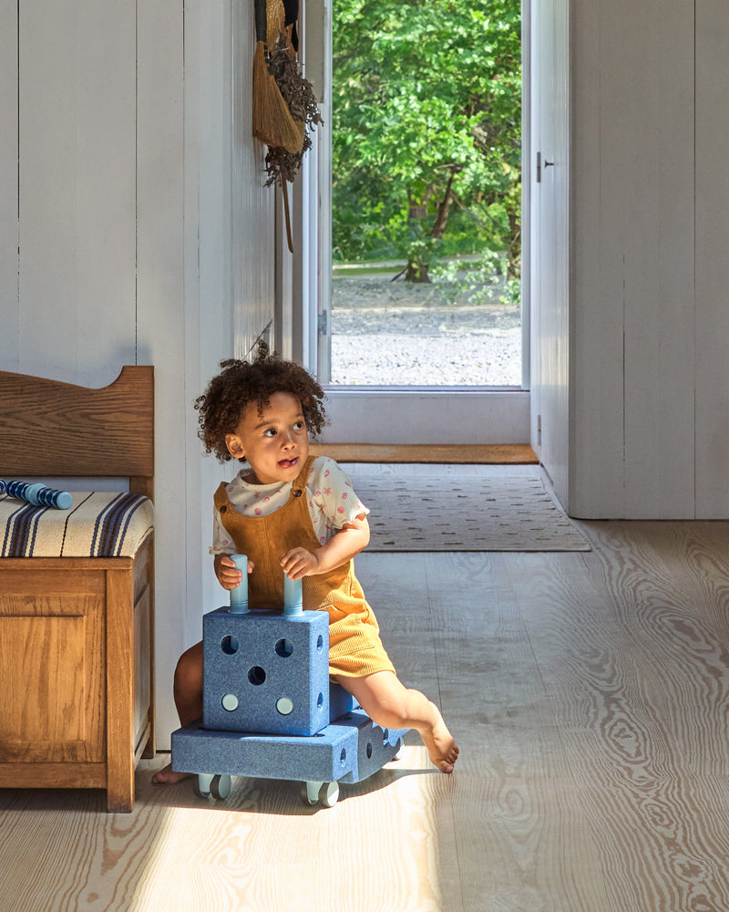 A child plays indoors riding a ride-on toy car build from the MODU Curiosity Set in deep blue.