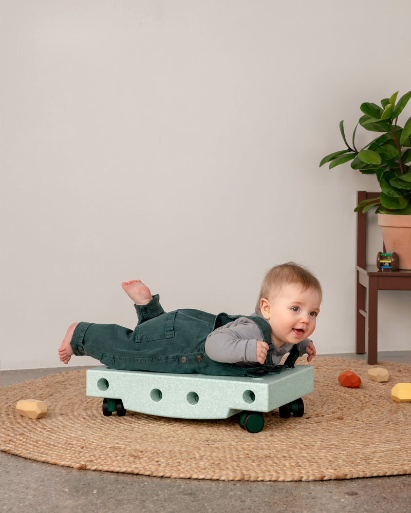 Baby macht Bauchlage auf dem MODU Scooter Board aus dem Curiosity Set in der Farbe Ocean Mint Forest Green.