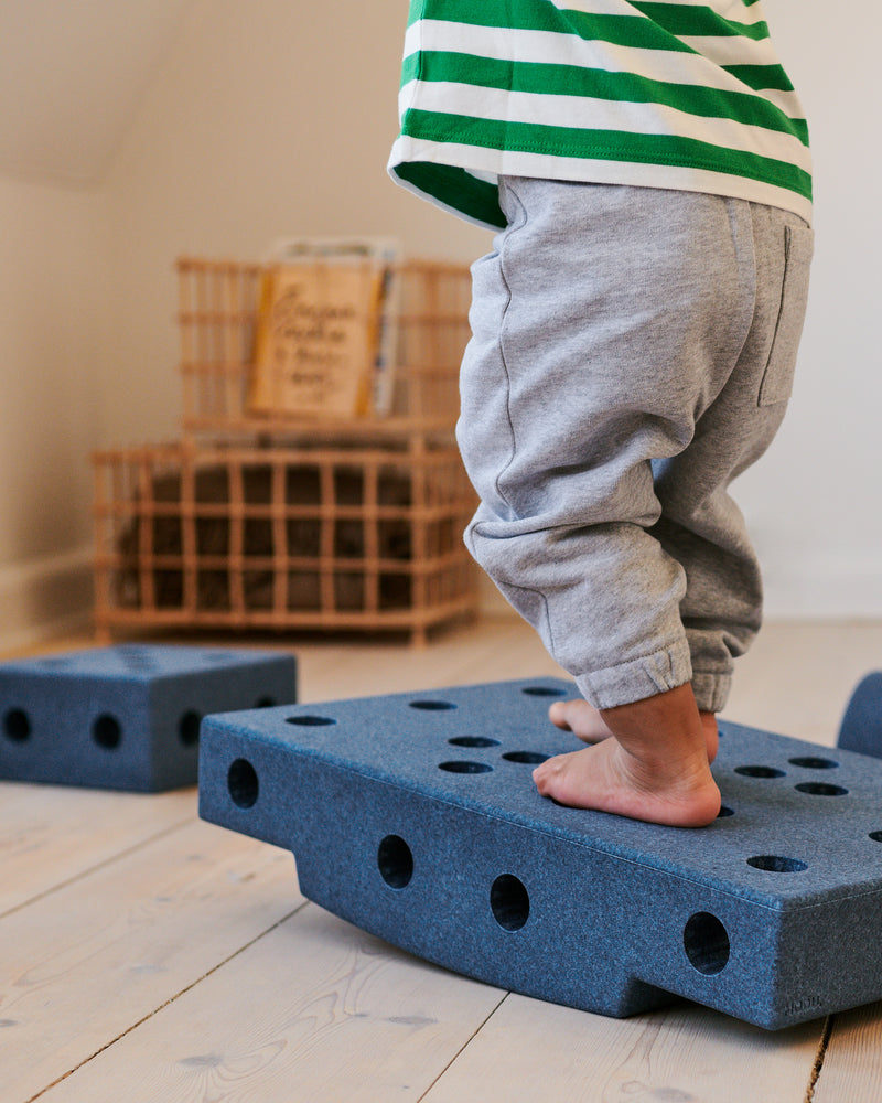 A close-up of a child balancing on deep blue MODU foam blocks during active play indoors.