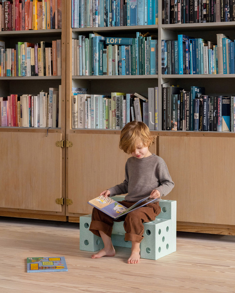 A child sits in front of a bookcase reading a book on a small ocean mint toddler bench built from the MODU Explorer Set.