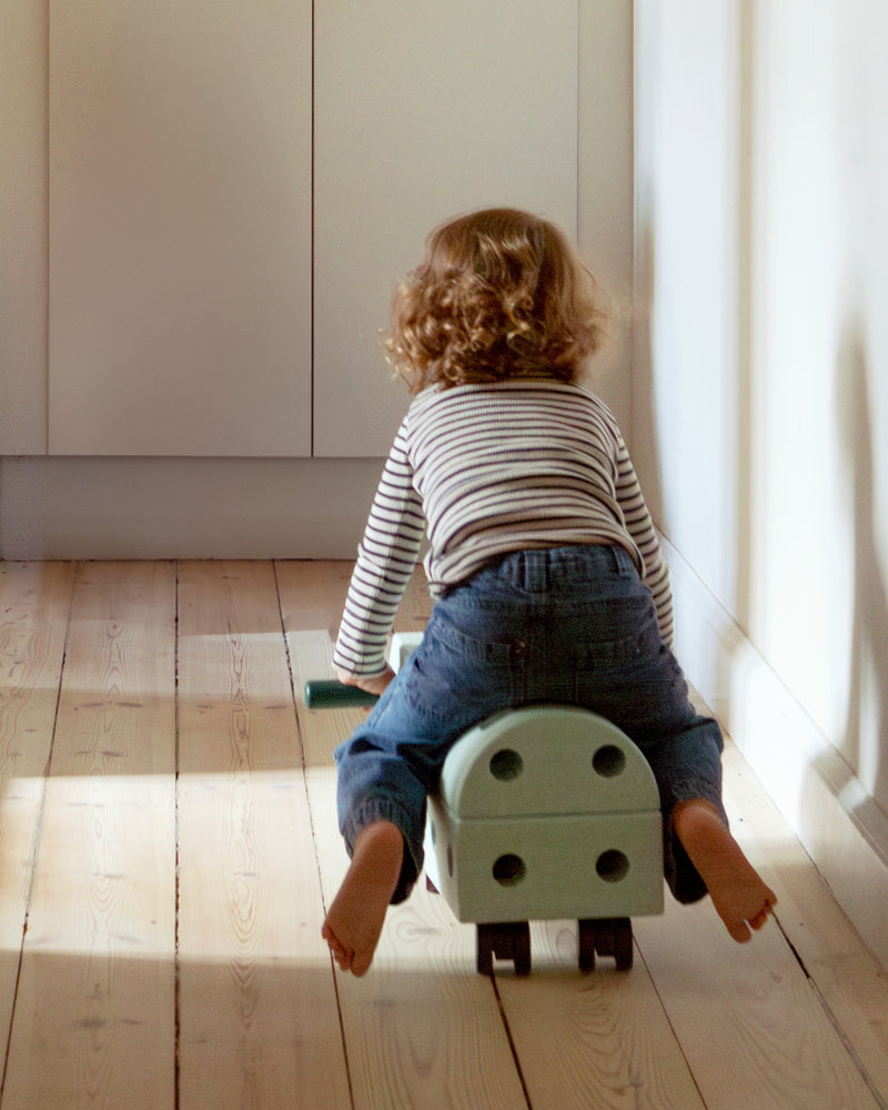 From a back view, a child rides down a hallway on an ocean mint ride-on toy car built from the MODU Explorer Set.