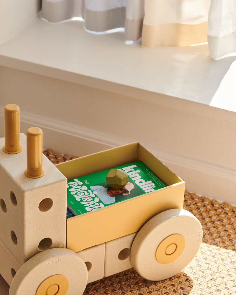 A honey yellow MODU Folding Box integrated into a push toy, holding a book and toy blocks.