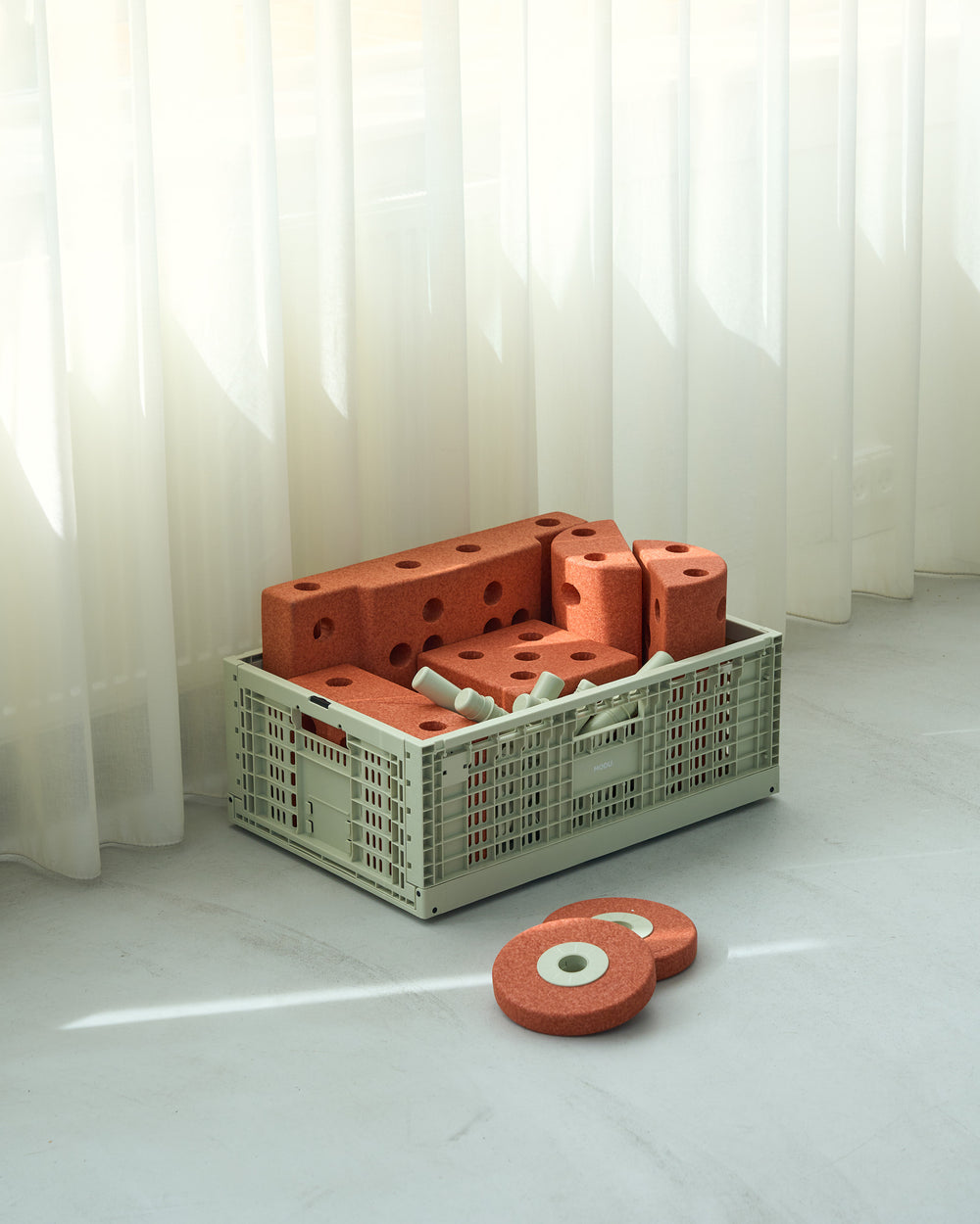 Orange MODU blocks and a crate on a white floor with sheer curtains in the background