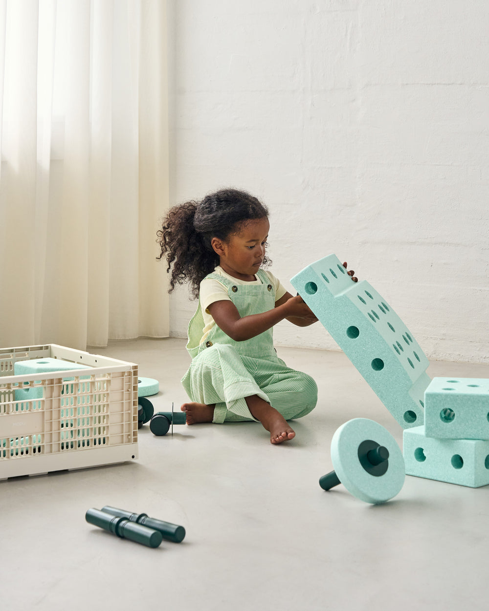 Child playing with mint MODU building blocks on a light-colored floor.