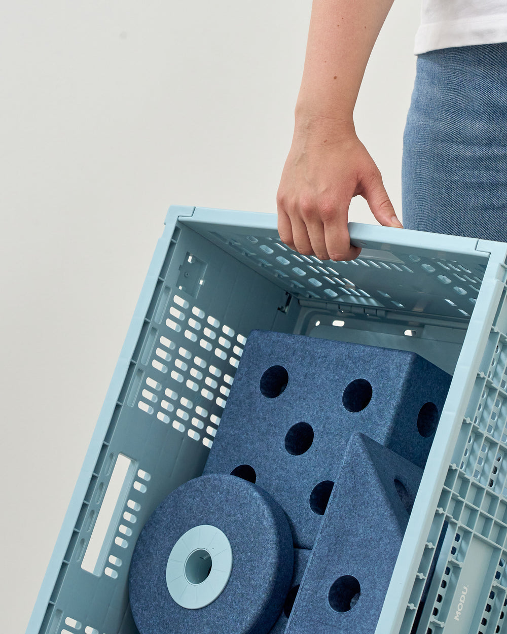 Person holding a blue storage crate with foam blocks inside on a light gray background
