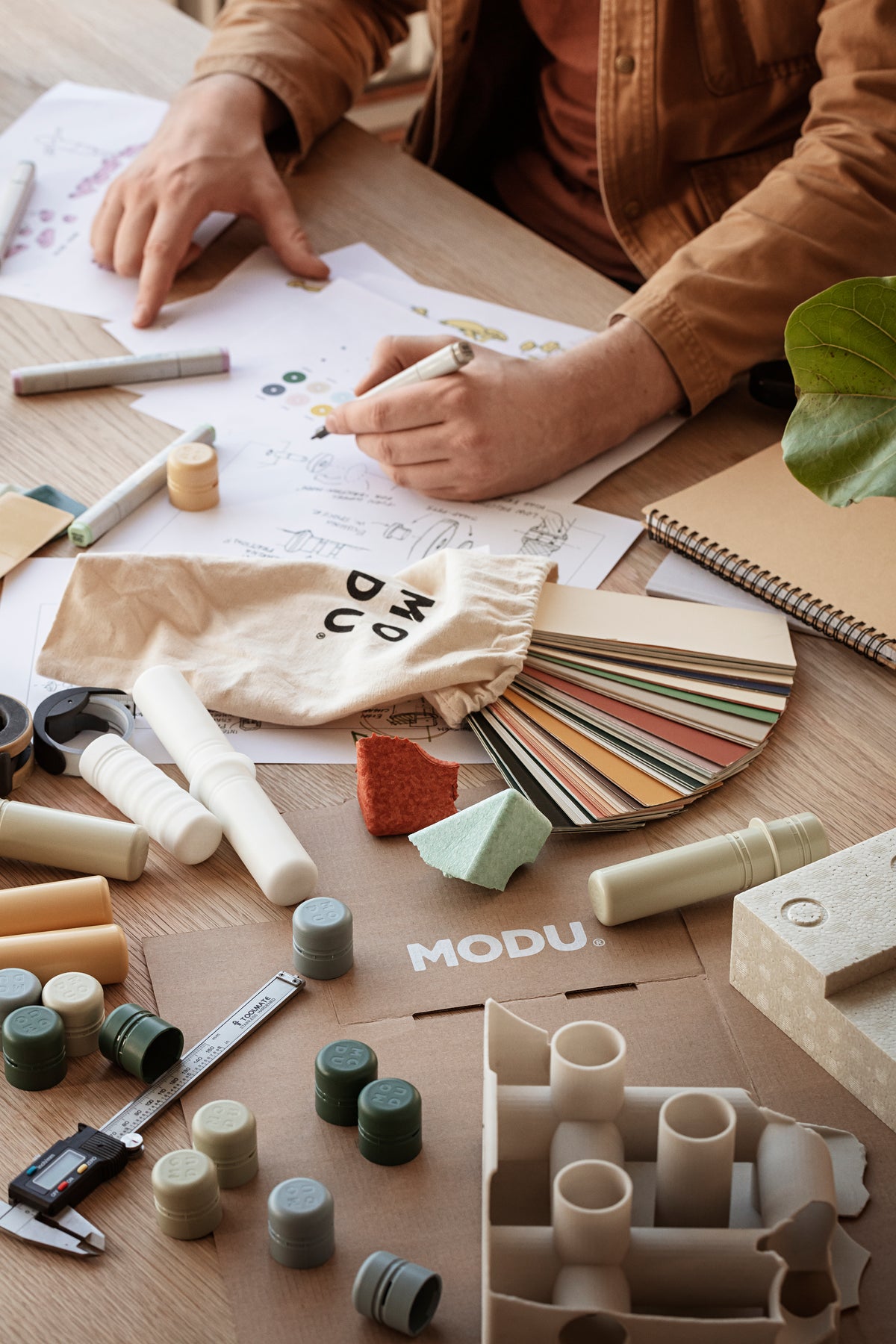 Product developer sketching new MODU product with material samples and sketches on desk.