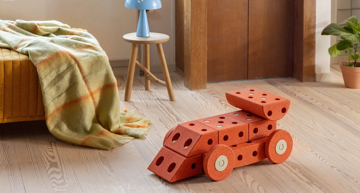MODU racecar ride on toy styled in kids room. Product color: Burnt Orange Dusty Green.