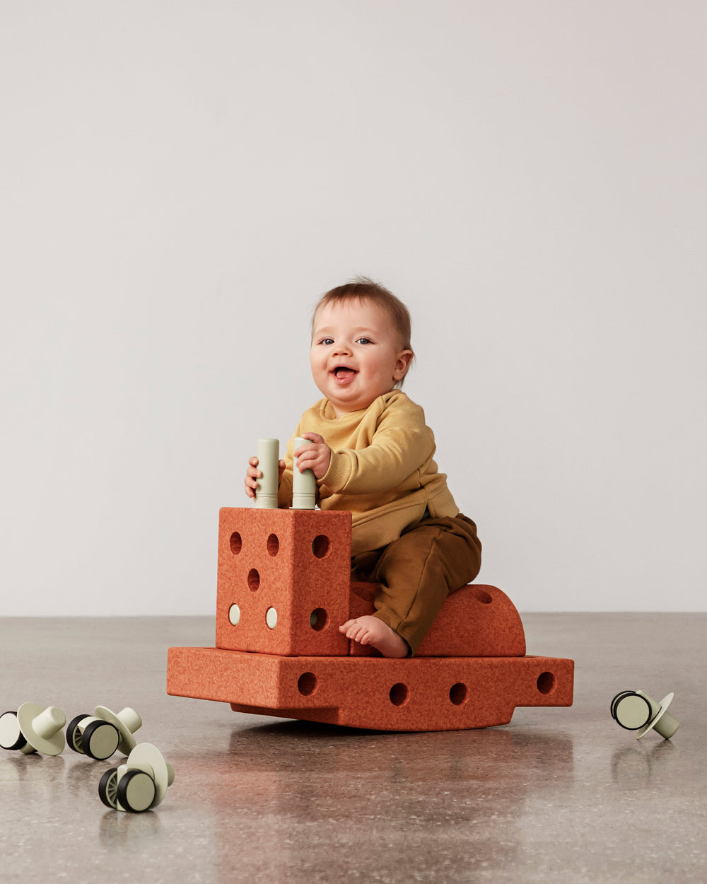 Baby having fun riding MODU rocker, practicing balance skills. Built from Curiosity Set in Burnt Orange Dusty Green.