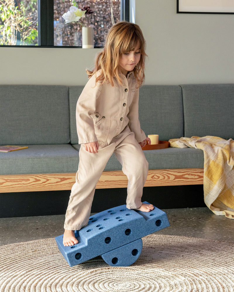 Kleinkind spielt im Wohnzimmer auf einem MODU Balance Board aus dem Curiosity Set in der Farbe Deep Blue Sky Blue.