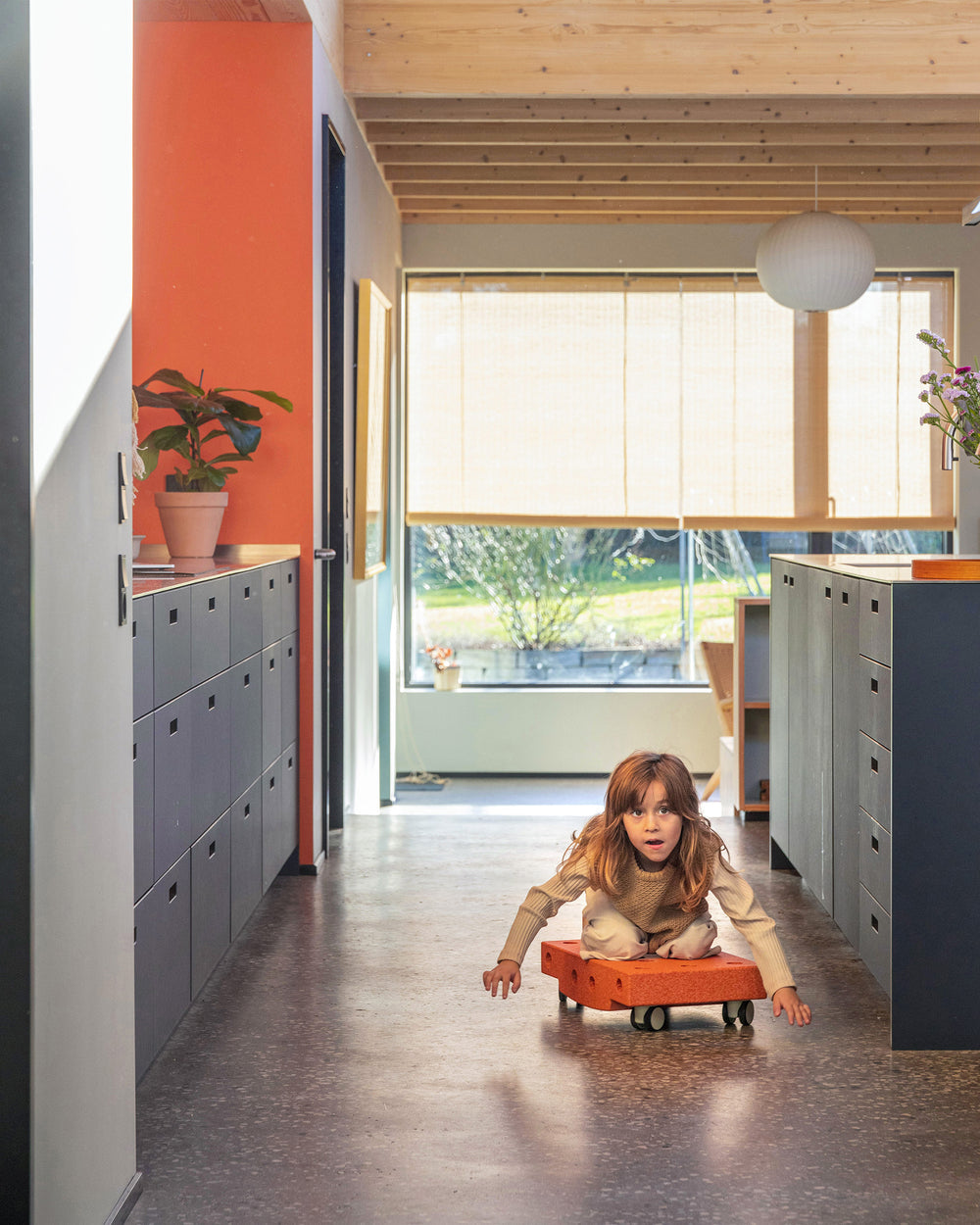Toddler riding on MODU Scooter Board in Burnt Orange Dusty Green. Encourages active play.