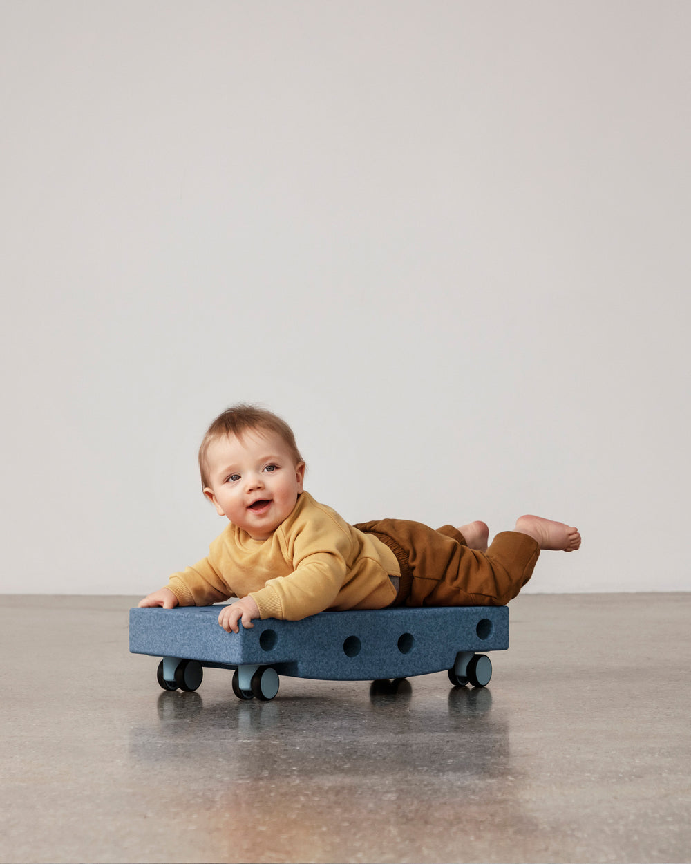 Baby playing on MODU Scooter Board in Deep Blue Sky Blue. Encourages motor skill development.