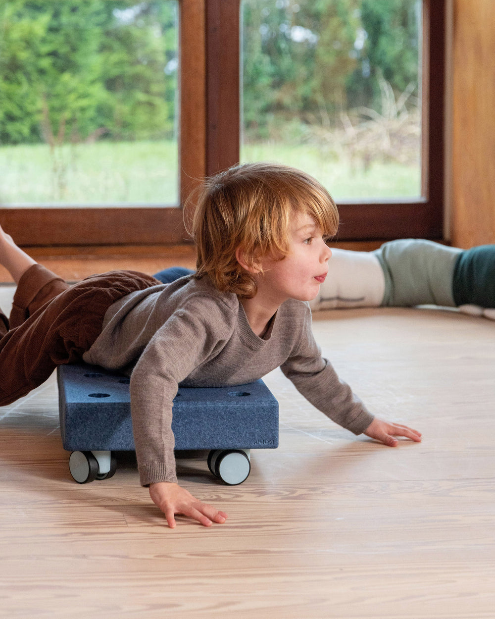 Toddler playing in the living room on MODU Scooter Board in Deep Blue Sky Blue. Encourages active play.