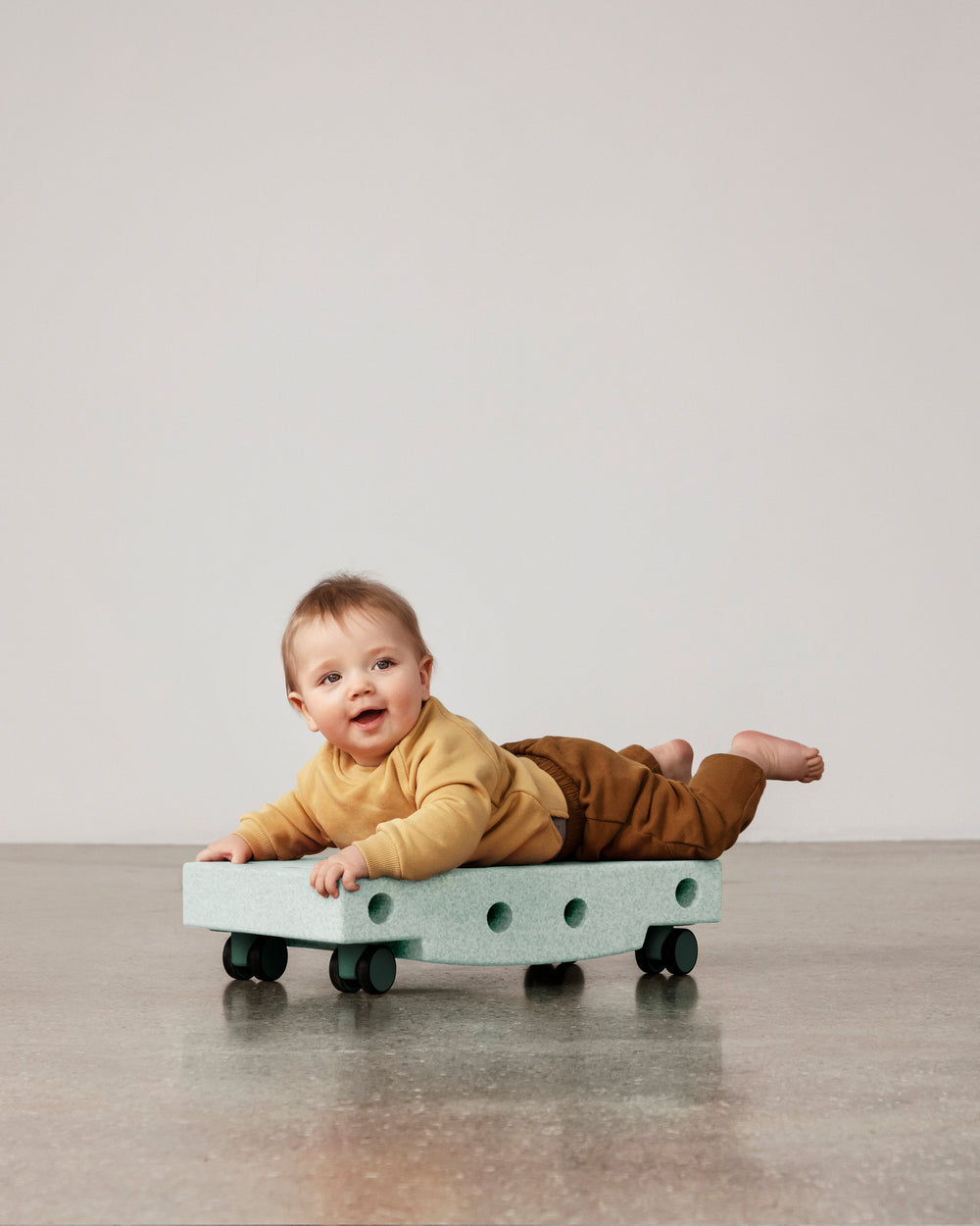 Baby playing on MODU Scooter Board in Ocean Mint Forest Green. Encourages motor skill development.