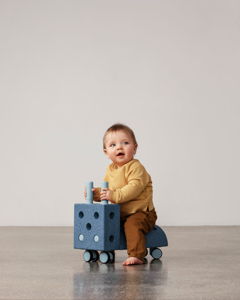 A young toddler rides a deep blue sky-blue MODU Tiny Ride.