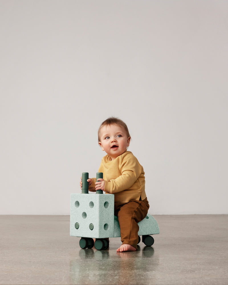 A young toddler rides a ocean mint forrest green MODU Tiny Ride.