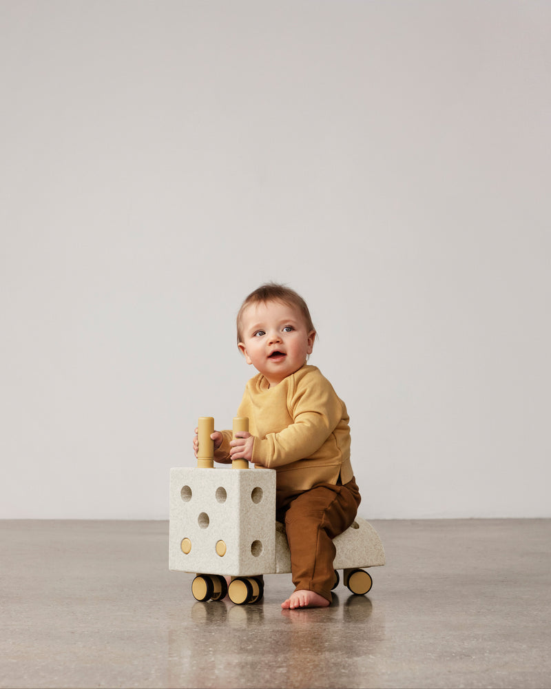 A young toddler rides a sand grey and honey yellow MODU Tiny Ride.