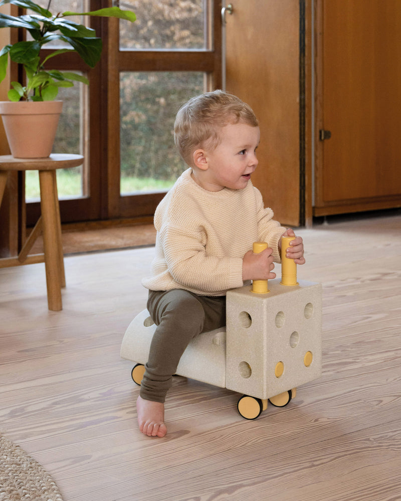 A young toddler rides a sand grey and honey yellow MODU Tiny Ride.